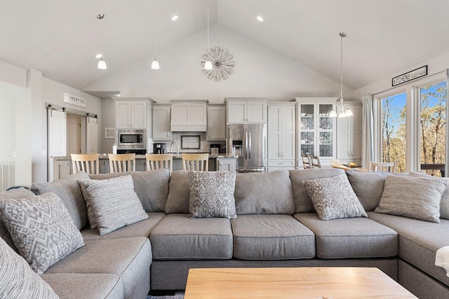 living room with a notable chandelier, sink, high vaulted ceiling, and a barn door