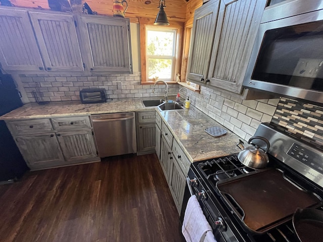 kitchen with pendant lighting, sink, stainless steel appliances, light stone countertops, and dark hardwood / wood-style flooring