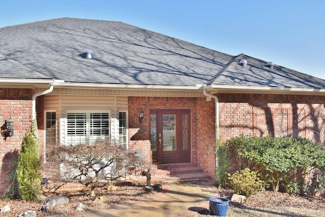 doorway to property with brick siding and a shingled roof