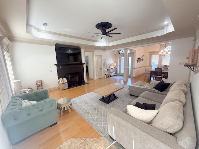 living room with ceiling fan, hardwood / wood-style floors, decorative columns, a tray ceiling, and a large fireplace