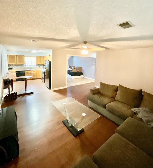 living room with ceiling fan, light hardwood / wood-style floors, and a textured ceiling