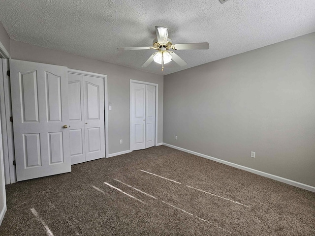 unfurnished bedroom with dark carpet, two closets, a textured ceiling, and ceiling fan