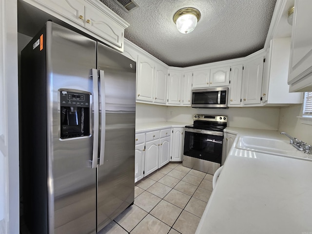 kitchen featuring sink, light tile patterned floors, appliances with stainless steel finishes, a textured ceiling, and white cabinets