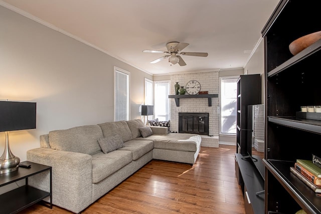 living room featuring hardwood / wood-style flooring, ceiling fan, ornamental molding, and a brick fireplace