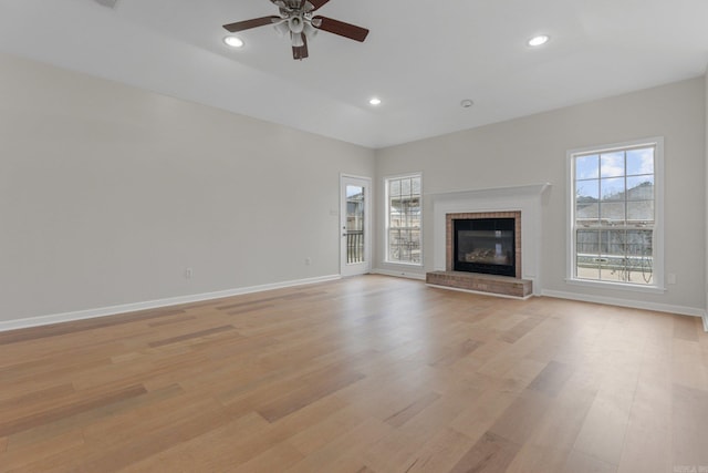 unfurnished living room featuring ceiling fan, a brick fireplace, and light hardwood / wood-style flooring