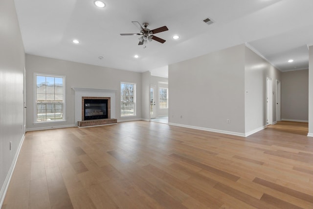 unfurnished living room with crown molding, ceiling fan, a brick fireplace, and light wood-type flooring