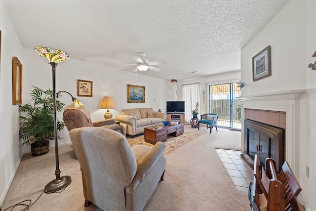 living room with a tile fireplace, light colored carpet, ceiling fan, and a textured ceiling