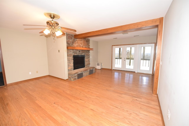 unfurnished living room featuring light hardwood / wood-style flooring, ceiling fan, beam ceiling, a stone fireplace, and french doors