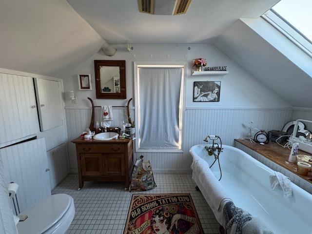 bathroom with toilet, vanity, a bathtub, vaulted ceiling with skylight, and tile patterned flooring