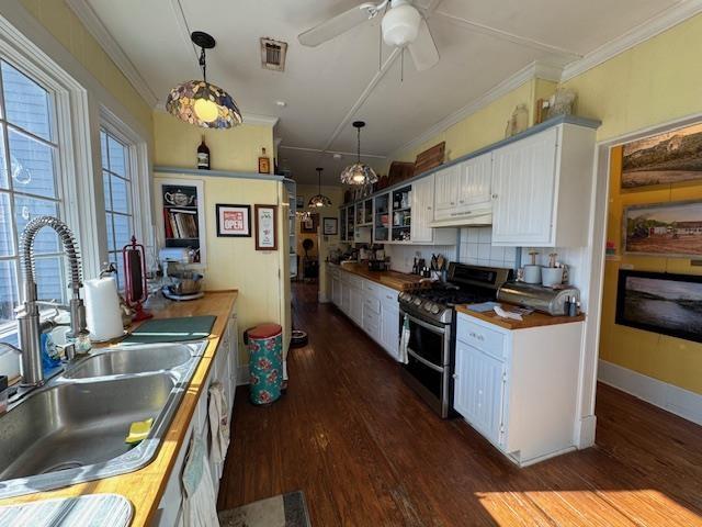 kitchen featuring butcher block countertops, sink, hanging light fixtures, white cabinets, and range with two ovens