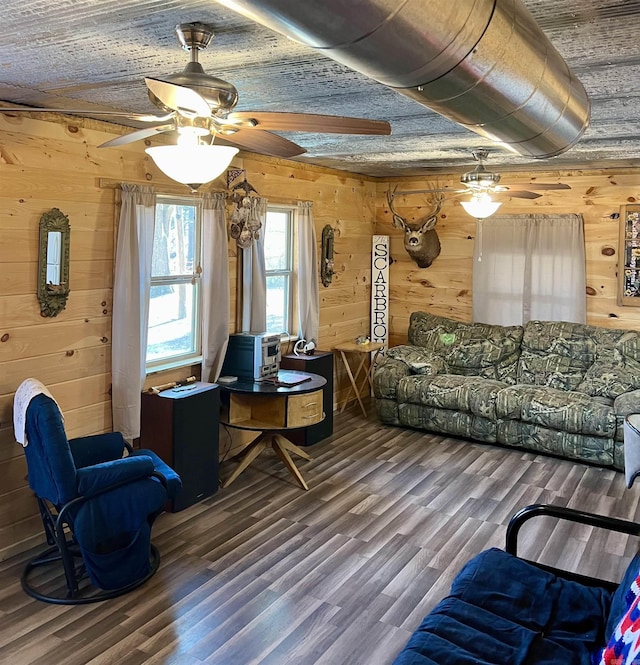 living room with dark wood-type flooring, ceiling fan, and wooden walls