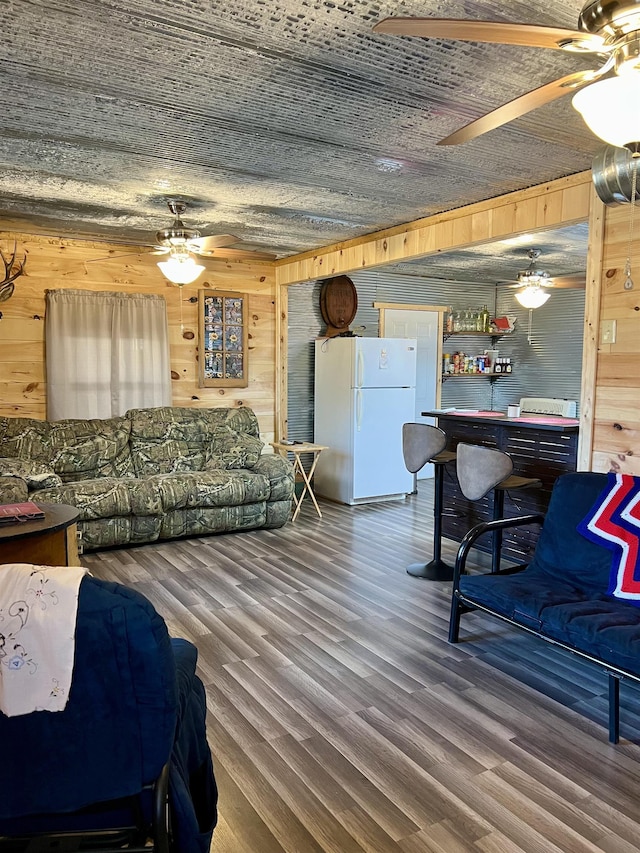 living room featuring wood-type flooring, ceiling fan, bar area, and wooden walls