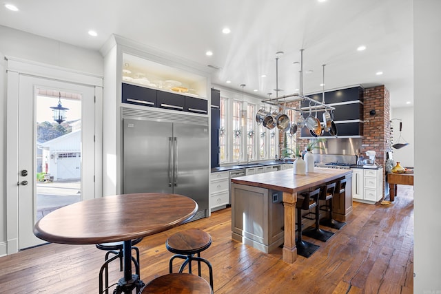 kitchen featuring wooden counters, white cabinetry, hanging light fixtures, a kitchen island, and built in fridge