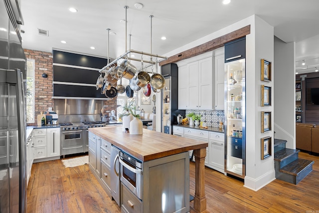 kitchen featuring appliances with stainless steel finishes, a kitchen island, tasteful backsplash, white cabinetry, and wooden counters