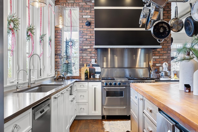 kitchen featuring wood counters, dishwasher, sink, white cabinets, and high end stainless steel range oven