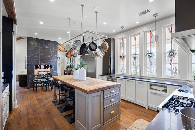 kitchen with wood counters, sink, white cabinetry, a center island, and hanging light fixtures