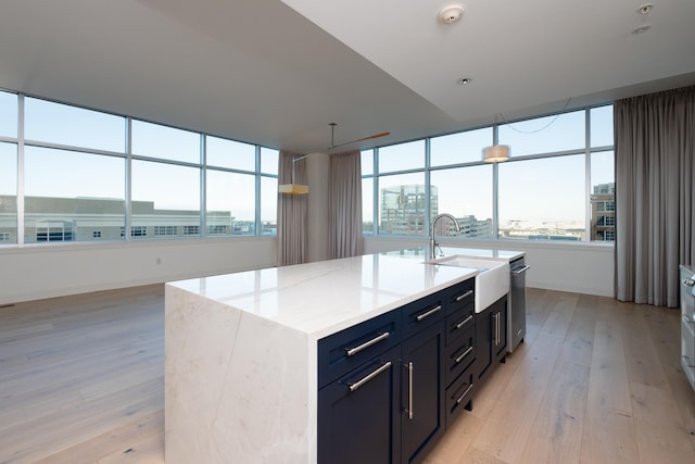 kitchen with a kitchen island with sink, sink, light stone countertops, and light wood-type flooring