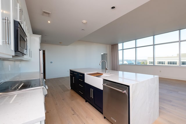 kitchen featuring sink, light hardwood / wood-style flooring, a kitchen island with sink, stainless steel appliances, and white cabinets