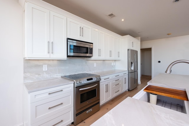 kitchen featuring appliances with stainless steel finishes, light stone counters, light hardwood / wood-style floors, white cabinets, and decorative backsplash