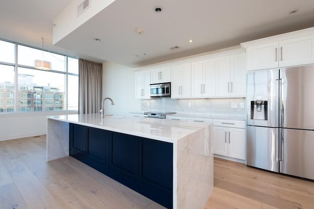 kitchen featuring sink, appliances with stainless steel finishes, white cabinetry, a kitchen island with sink, and tasteful backsplash