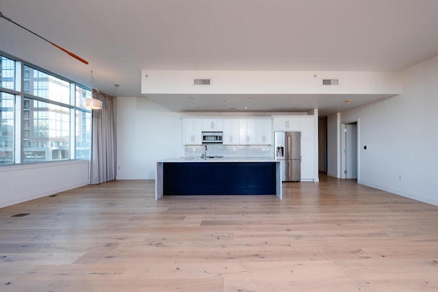 kitchen featuring light wood-type flooring, white cabinets, stainless steel appliances, a kitchen island with sink, and backsplash