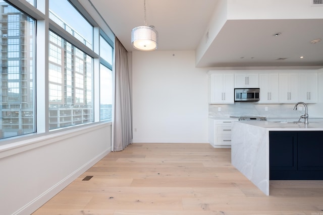 kitchen featuring pendant lighting, sink, light hardwood / wood-style flooring, white cabinets, and decorative backsplash