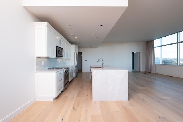 kitchen with sink, light wood-type flooring, white cabinets, stainless steel appliances, and backsplash