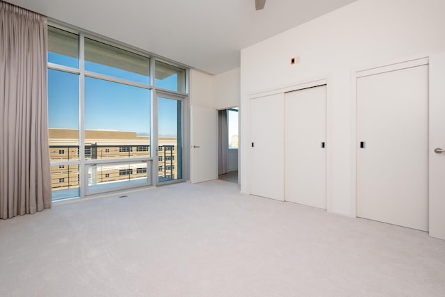 unfurnished bedroom with floor to ceiling windows, two closets, and light carpet