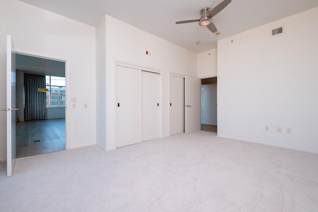 unfurnished bedroom featuring multiple closets, ceiling fan, and light carpet