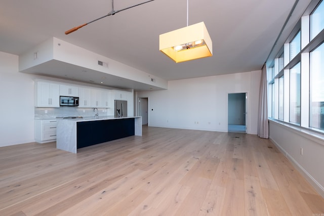 kitchen featuring appliances with stainless steel finishes, a kitchen island with sink, white cabinets, decorative backsplash, and light wood-type flooring