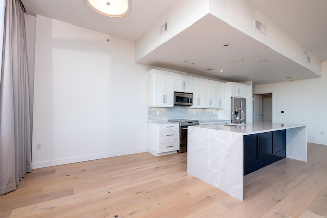 kitchen featuring decorative backsplash, appliances with stainless steel finishes, a center island with sink, and white cabinets