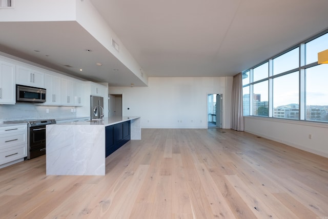 kitchen with white cabinetry, stainless steel appliances, an island with sink, and decorative backsplash