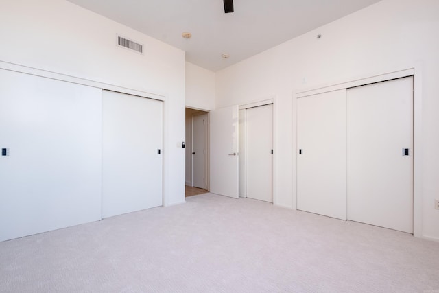 unfurnished bedroom with light carpet, two closets, and ceiling fan