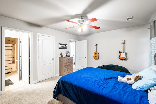 bedroom with ensuite bathroom, light colored carpet, and ceiling fan