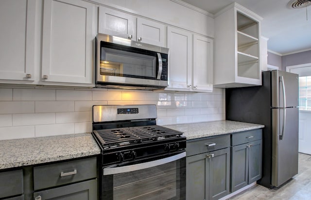 kitchen with gray cabinetry, stainless steel appliances, light stone countertops, light hardwood / wood-style floors, and backsplash