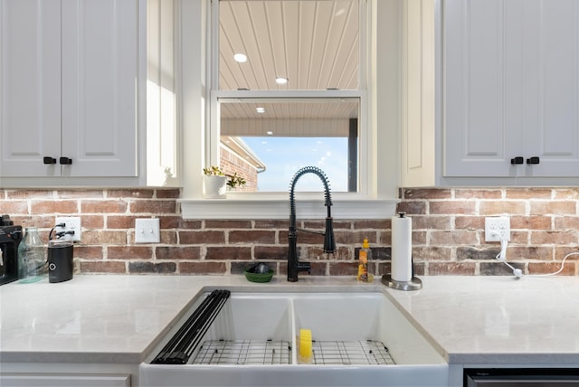 interior details featuring white cabinetry, dishwashing machine, light stone countertops, and sink
