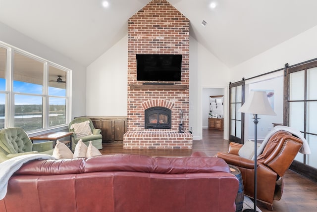 living room featuring vaulted ceiling, a barn door, dark hardwood / wood-style floors, and a brick fireplace