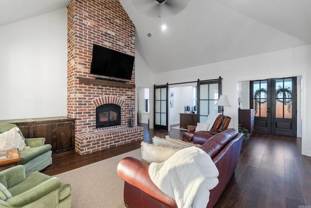living room featuring a fireplace, high vaulted ceiling, dark hardwood / wood-style flooring, a barn door, and french doors