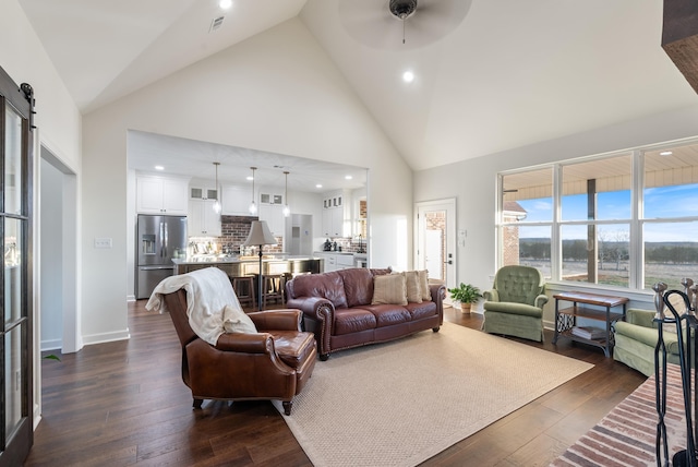 living room with dark hardwood / wood-style floors, high vaulted ceiling, a barn door, and ceiling fan