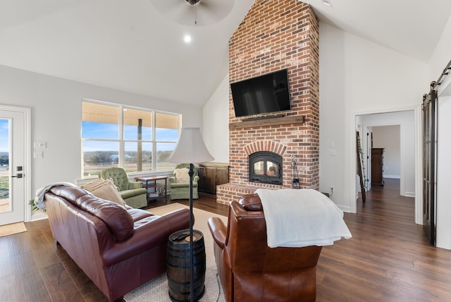 living room featuring dark hardwood / wood-style flooring, a barn door, high vaulted ceiling, and a fireplace