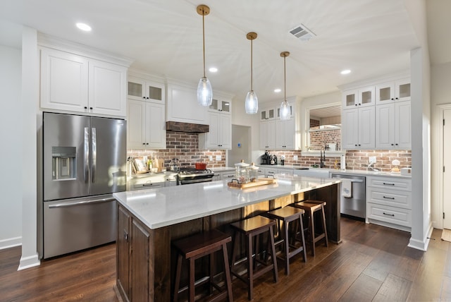 kitchen with hanging light fixtures, a kitchen island, stainless steel appliances, decorative backsplash, and white cabinets