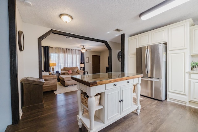 kitchen with a kitchen island, a textured ceiling, white cabinets, and stainless steel refrigerator