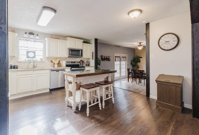 kitchen featuring a breakfast bar area, stainless steel appliances, dark hardwood / wood-style floors, a textured ceiling, and white cabinets