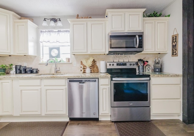 kitchen with appliances with stainless steel finishes, dark hardwood / wood-style floors, sink, decorative backsplash, and light stone counters