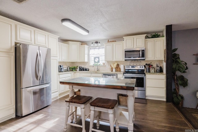 kitchen with sink, a center island, a textured ceiling, stainless steel appliances, and light hardwood / wood-style floors