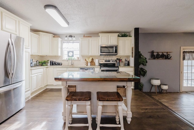 kitchen featuring sink, light hardwood / wood-style flooring, stainless steel appliances, a center island, and a textured ceiling