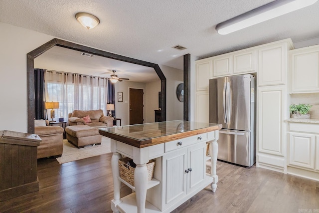 kitchen with white cabinetry, light hardwood / wood-style flooring, stainless steel refrigerator, and a textured ceiling