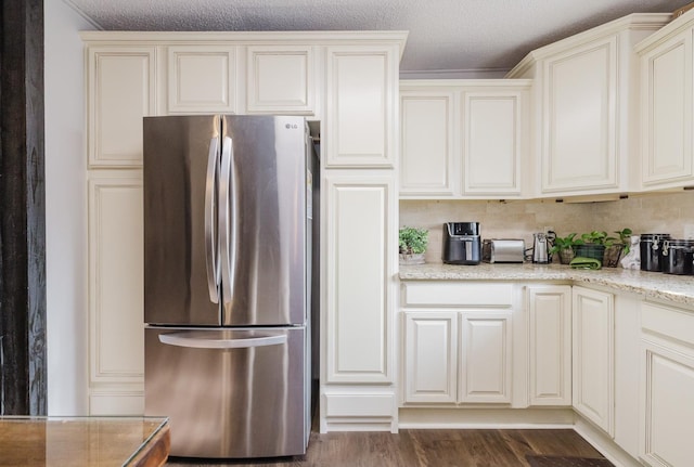 kitchen with dark wood-type flooring, stainless steel fridge, cream cabinets, light stone countertops, and a textured ceiling