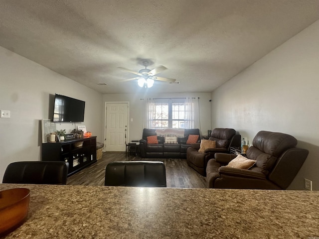 living room featuring dark hardwood / wood-style flooring, ceiling fan, and a textured ceiling