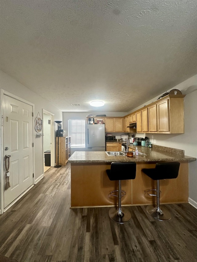 kitchen with stainless steel fridge, kitchen peninsula, a textured ceiling, and light brown cabinets